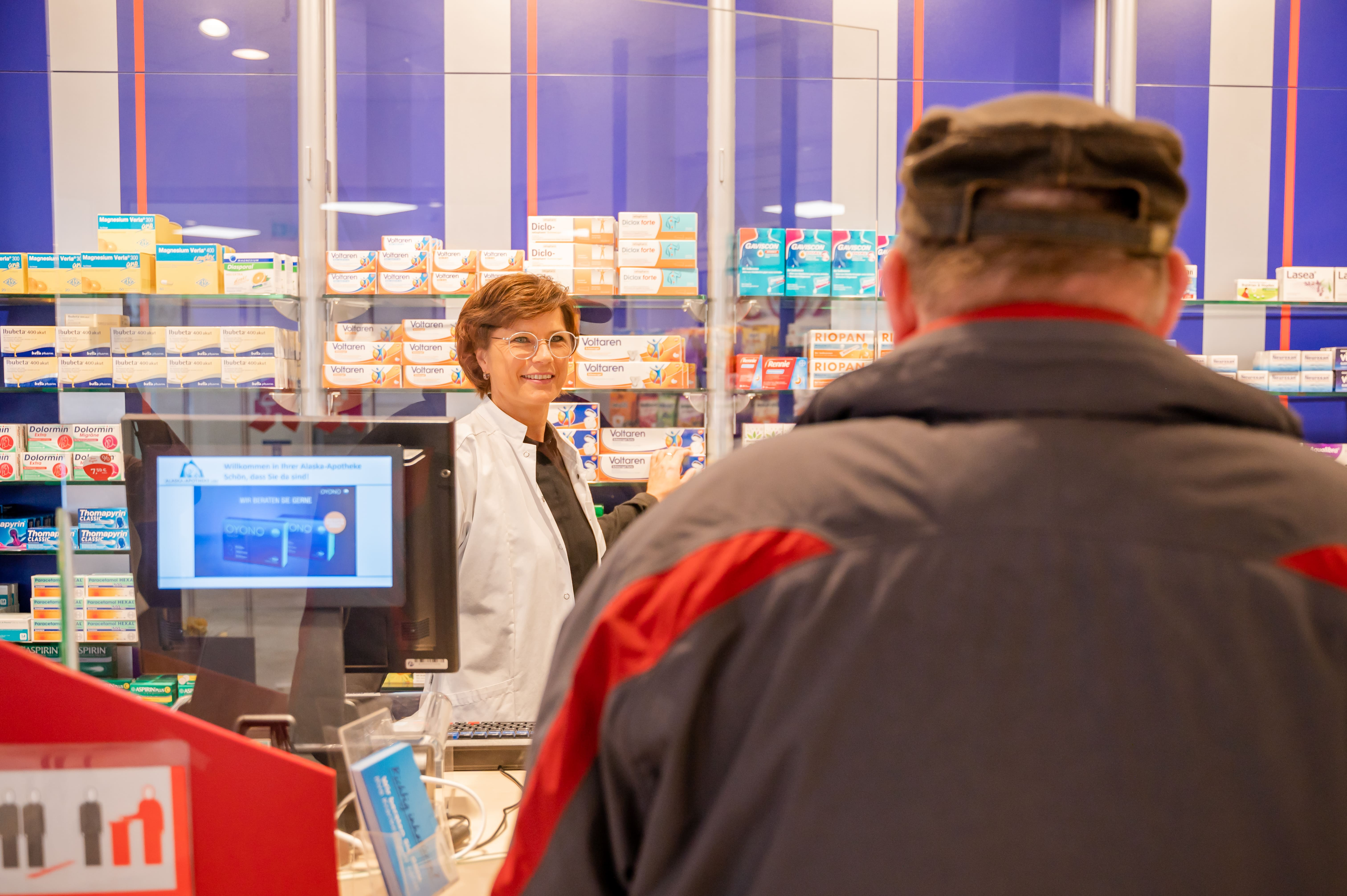 Mitarbeiterin hinter der Kassen und Kunde den sie begrüßt